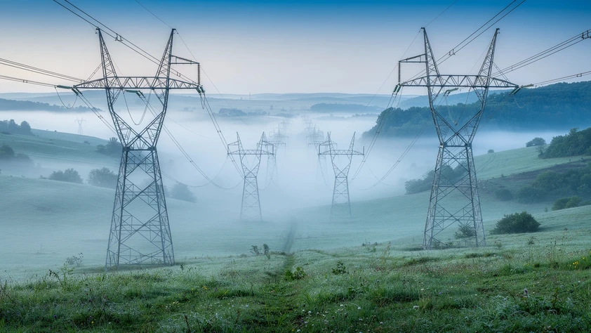 Pylônes électriques à haute tension traversant une vallée verdoyante dans la brume du matin