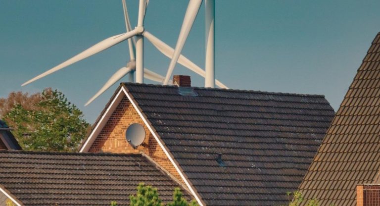 Éoliennes visibles derrière les toits d'un quartier résidentiel