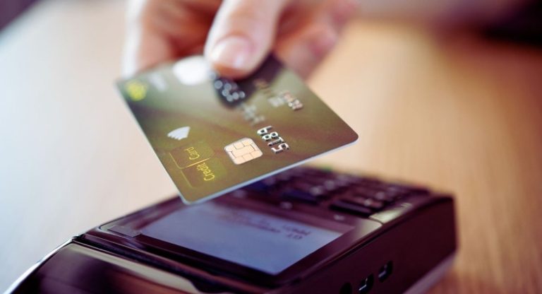 Main approchant une carte bancaire d'un terminal de paiement sans contact