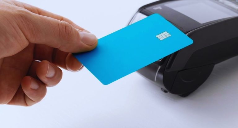 Main tenant une carte bleue devant un terminal de paiement sans contact
