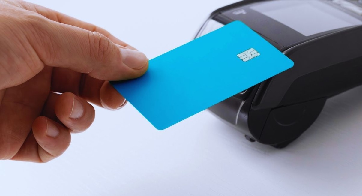 Main tenant une carte bleue devant un terminal de paiement sans contact