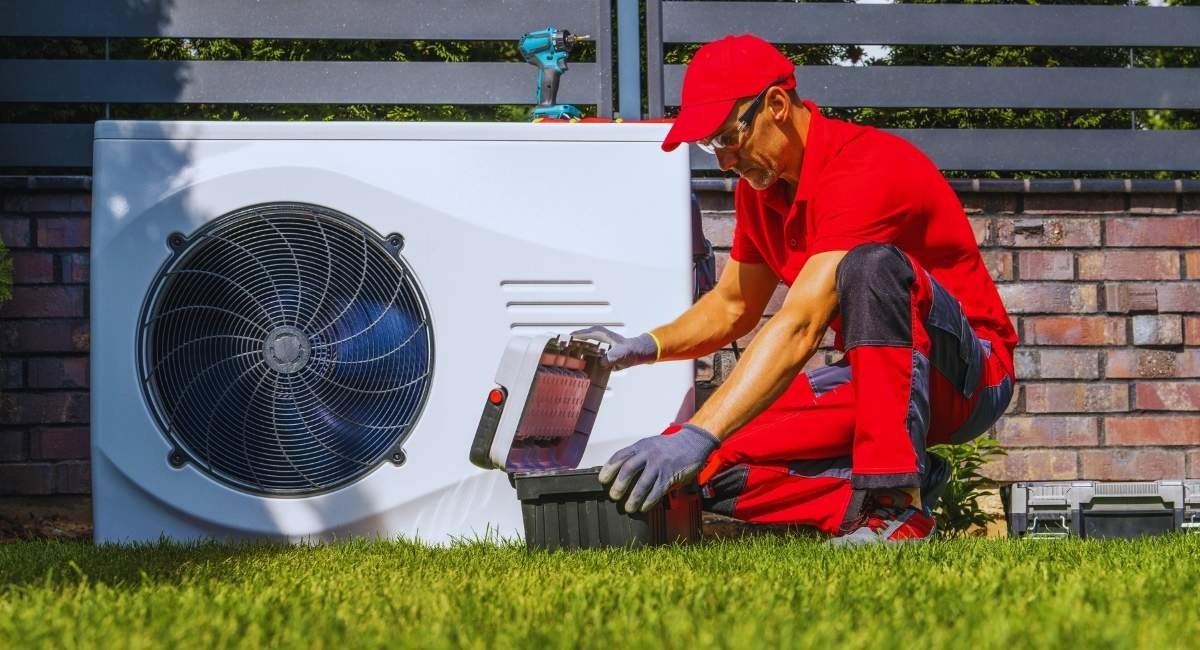 Technicien en tenue rouge s'occupant d'une pompe à chaleur installée dans un jardin